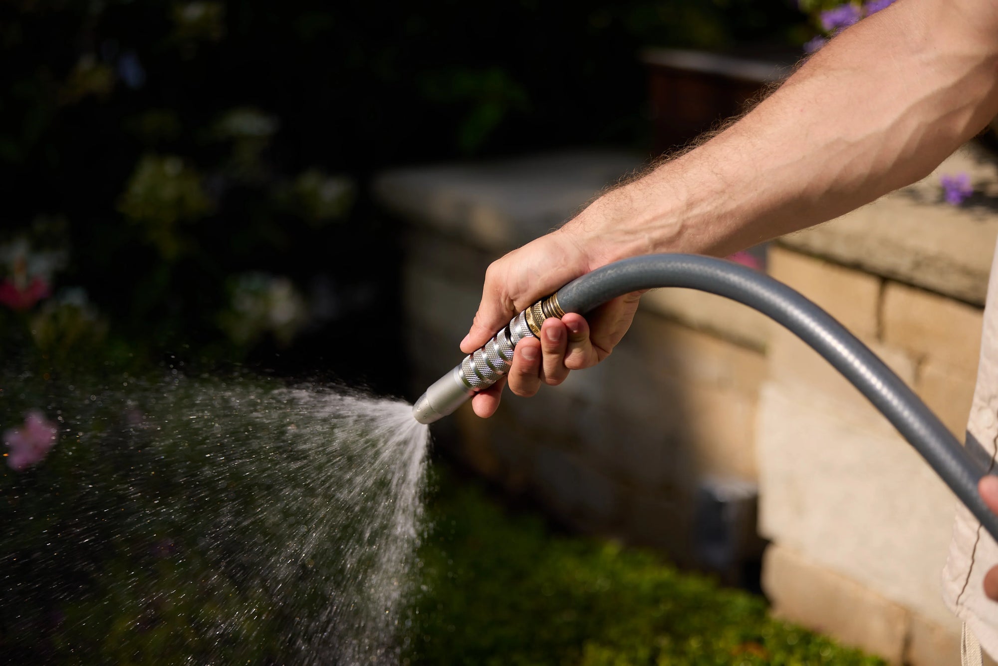 Hand holding stainless steel spray nozzle, spraying water in garden setting