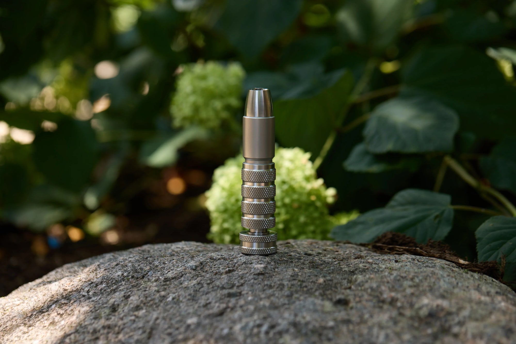Stainless steel spray nozzle standing on a rock outdoors with greenery in the background